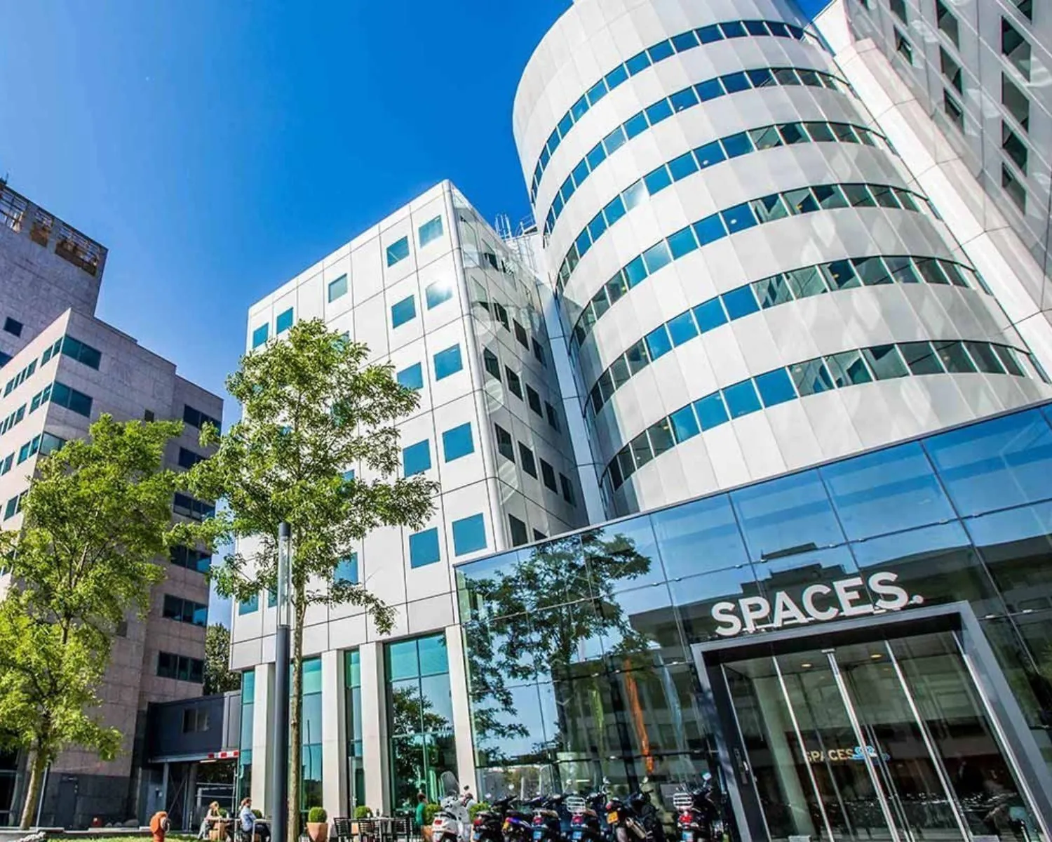 Moderne kantoorgebouwen met de ingang van het bedrijfsverzamelpand "Spaces" onder een blauwe lucht.