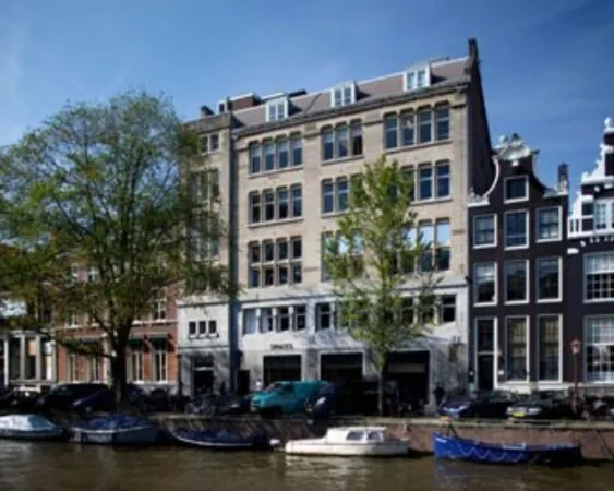 Gevel van het monumentale gebouw van Spaces aan de Herengracht in Amsterdam, met boten voor de deur aan de gracht.