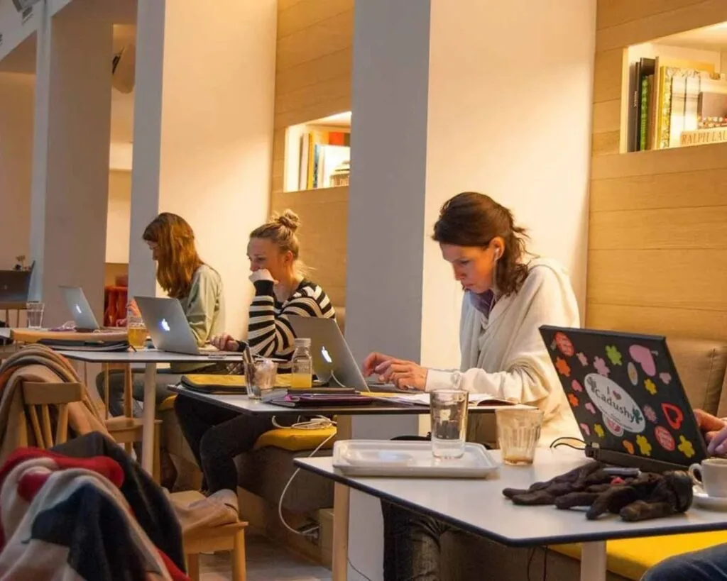 Mensen werken geconcentreerd op hun laptops in een modern café met gezellige verlichting.