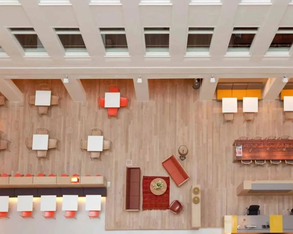 Bovenaanzicht van een modern, open kantoor of lobbyruimte met zitgedeeltes, tafels en stoelen in verschillende opstellingen.