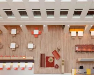 Bovenaanzicht van een modern, open kantoor of lobbyruimte met zitgedeeltes, tafels en stoelen in verschillende opstellingen.