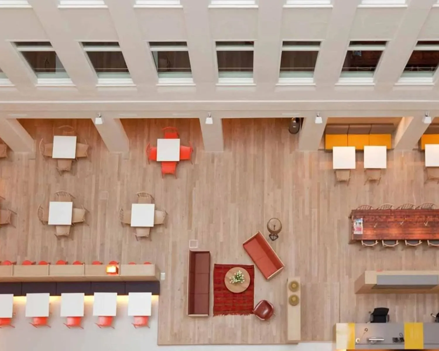 Bovenaanzicht van een modern, open kantoor of lobbyruimte met zitgedeeltes, tafels en stoelen in verschillende opstellingen.