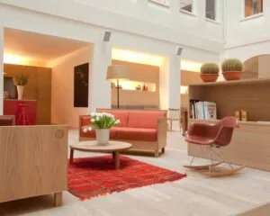 Modern ingerichte woonkamer met houten meubels, rode accenten en een rode schommelstoel op een licht houten vloer.