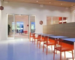 Moderne eetruimte met witte tafels, feloranje stoelen en een strakke, minimalistische inrichting.