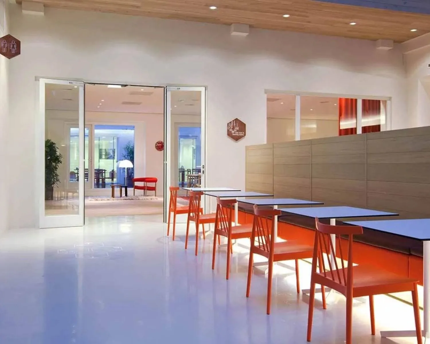 Moderne eetruimte met witte tafels, feloranje stoelen en een strakke, minimalistische inrichting.