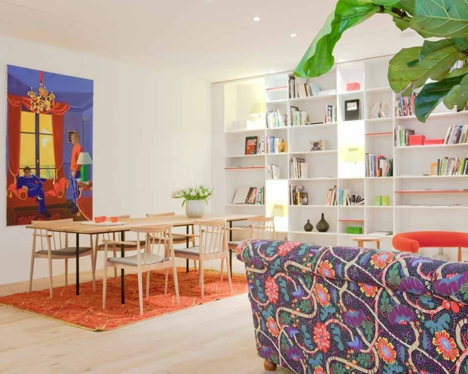 Kleurrijk ingerichte woonkamer met een boekenkast, eettafel, kunst aan de muur en een bank met bloemenpatroon.