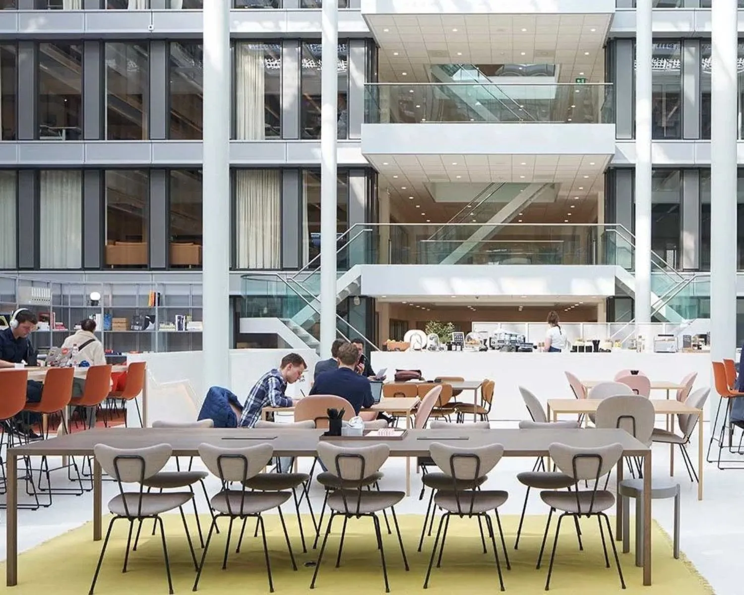 Moderne, open kantoorruimte met meerdere tafels, stoelen en mensen die werken of overleggen.