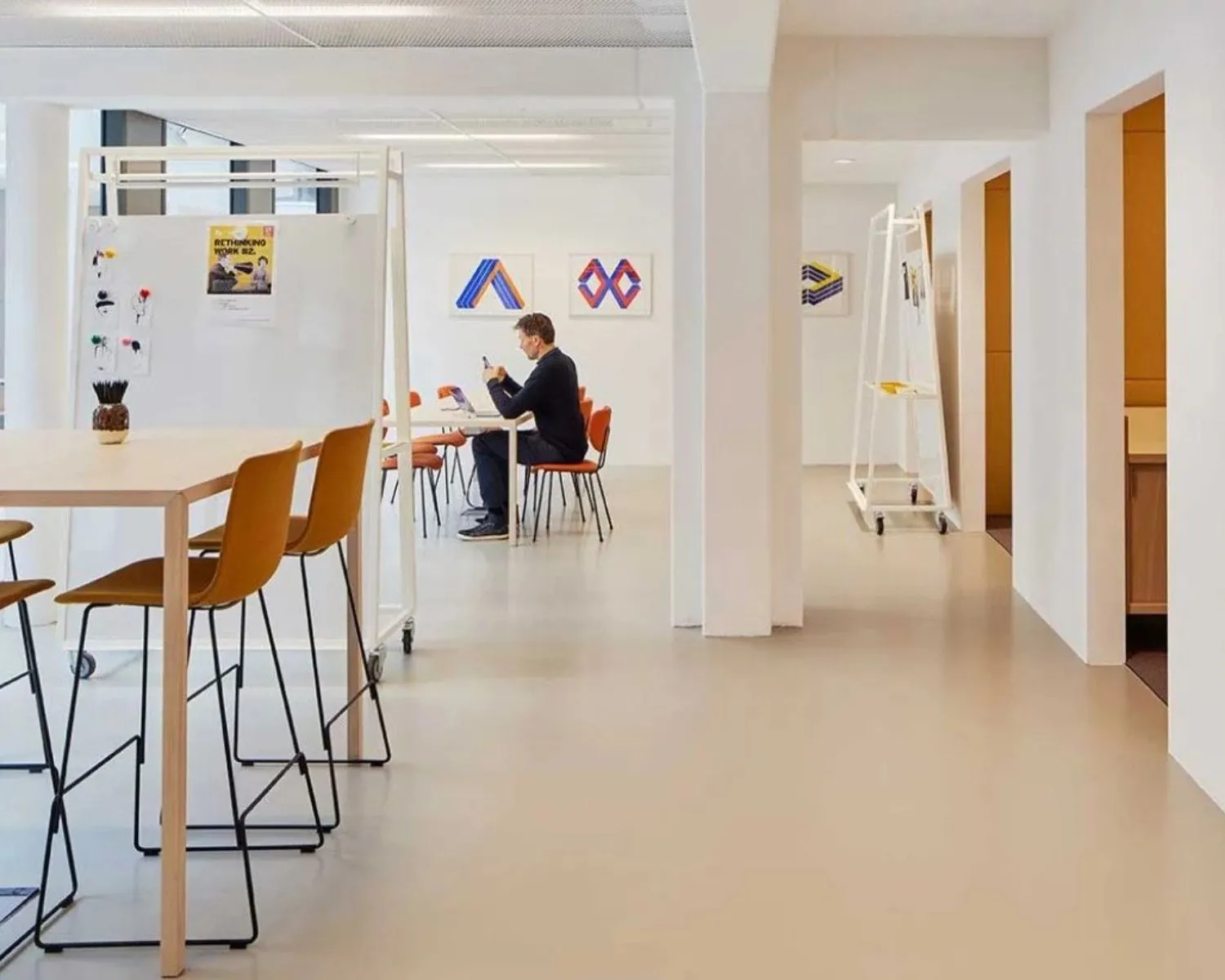 Moderne kantoorruimte met witte muren, oranje stoelen en een man die werkt aan een tafel met laptop.
