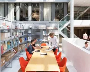 Moderne kantoorruimte met grote vergadertafel, open boekenrekken en mensen aan het werk.
