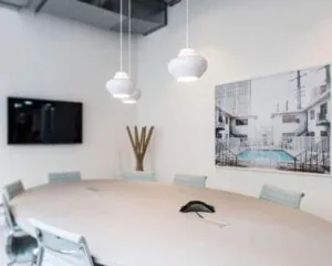 Moderne vergaderruimte met ovale tafel, hanglampen, flatscreen-tv en foto van een zwembad aan de muur.