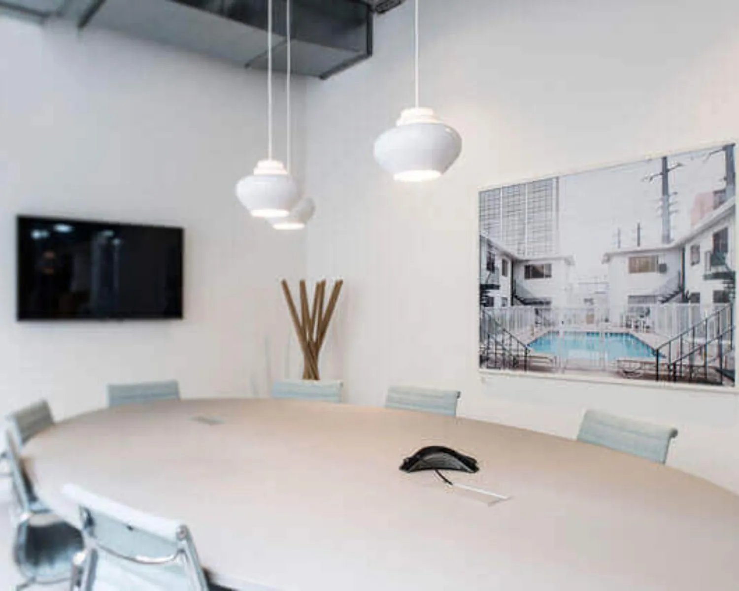 Moderne vergaderruimte met ovale tafel, hanglampen, flatscreen-tv en foto van een zwembad aan de muur.