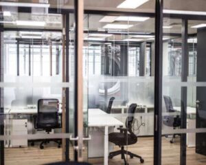 Moderne glazen kantoorruimte met meerdere lege bureaus en bureaustoelen.