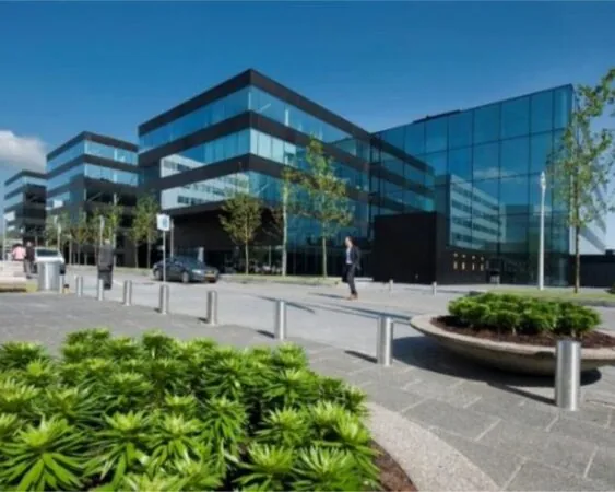 Modern kantoorgebouw met glazen gevels, omringd door groen en wandelpaden onder een heldere blauwe lucht.