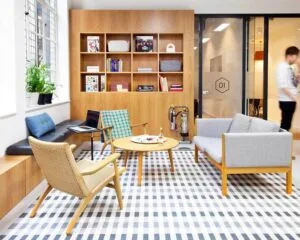 Moderne en lichte kantoorlounge met houten meubels, een boekenkast en een geruit vloerkleed.