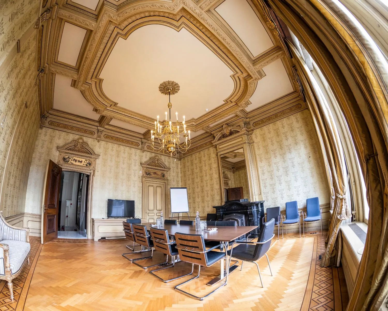 Vergaderruimte in klassieke stijl met een lange tafel, moderne stoelen, hoge plafonds en een kroonluchter.