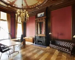 Luxe klassiek ingerichte kantoorruimte met houten lambrisering, leren bank, sierhaard en kroonluchter.