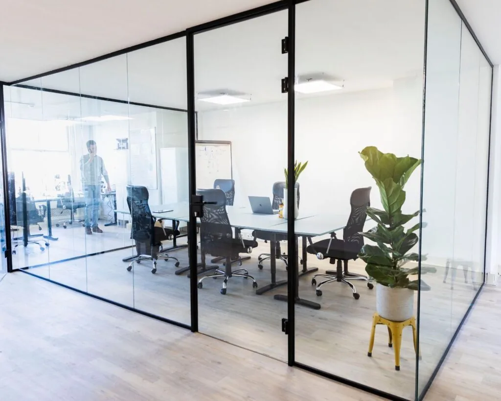 Moderne vergaderruimte met glazen wanden, vergadertafel, bureaustoelen en een grote kamerplant op de voorgrond.