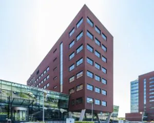 Modern roodbruin kantoorgebouw met glazen entree en meerdere verdiepingen, gefotografeerd op een heldere dag.