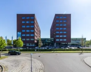 Modern rood bakstenen kantoorgebouw met een glazen entree en een bord "Te Huur" aan de gevel.