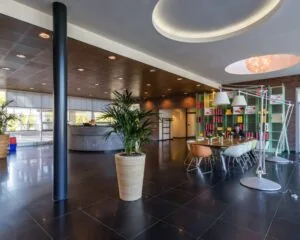 Moderne kantoorlobby met een receptiebalie, vergadertafel, kleurrijke stoelen en open boekenkasten tegen een bakstenen muur.