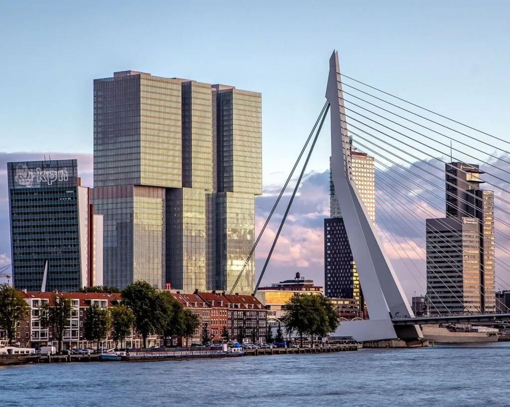 Zicht op de Erasmusbrug en de skyline van Rotterdam met het KPN-gebouw en De Rotterdam in de avondzon.
