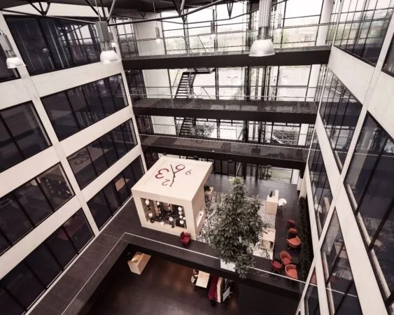 Open atrium van een modern kantoorgebouw met een grote kubusvormige klok en zitplekken op de begane grond.