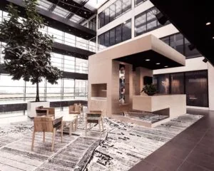 Moderne kantoorlobby met houten receptiemeubel, designstoelen, kunstige vloerkleden en een grote binnenboom.