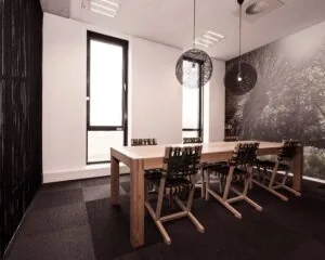Vergaderruimte met houten tafel, zes stoelen, moderne hanglampen en een natuurfoto als muurdecoratie.