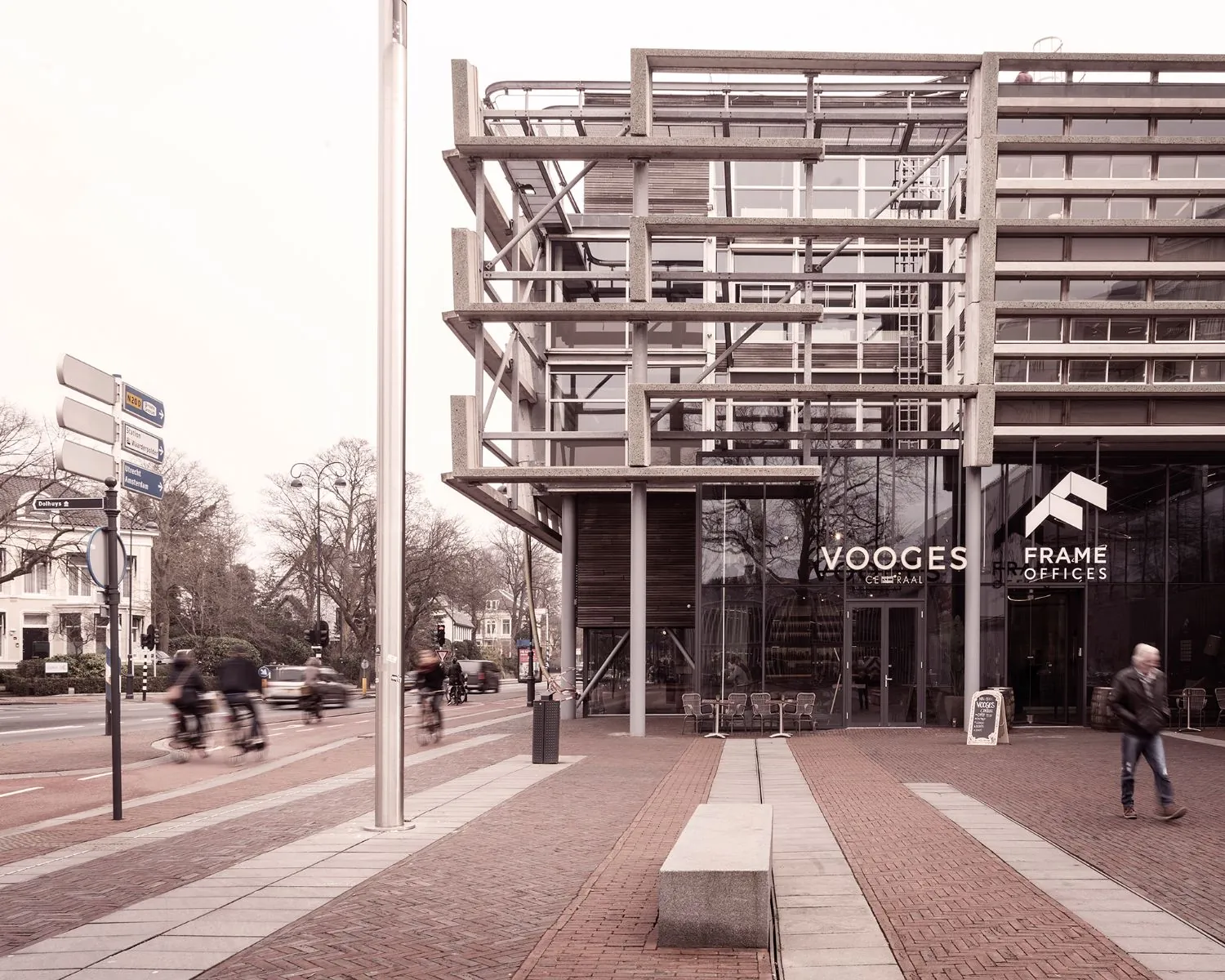 Moderne kantoorgevel met de namen "Vooges Centraal" en "Frame Offices" aan een druk kruispunt met fietsers en voetgangers.