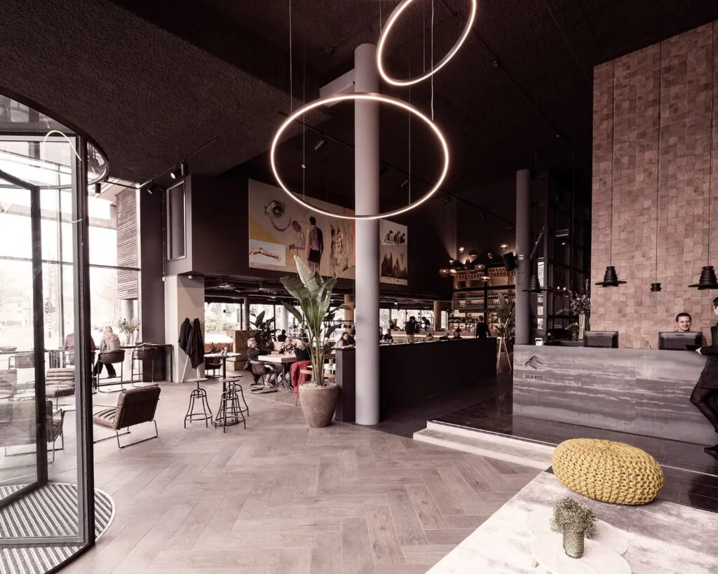 Modern ingericht hotel- of restaurantinterieur met hoge plafonds, een ronde lichtinstallatie en een receptiebalie.