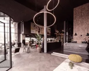 Modern ingericht hotel- of restaurantinterieur met hoge plafonds, een ronde lichtinstallatie en een receptiebalie.