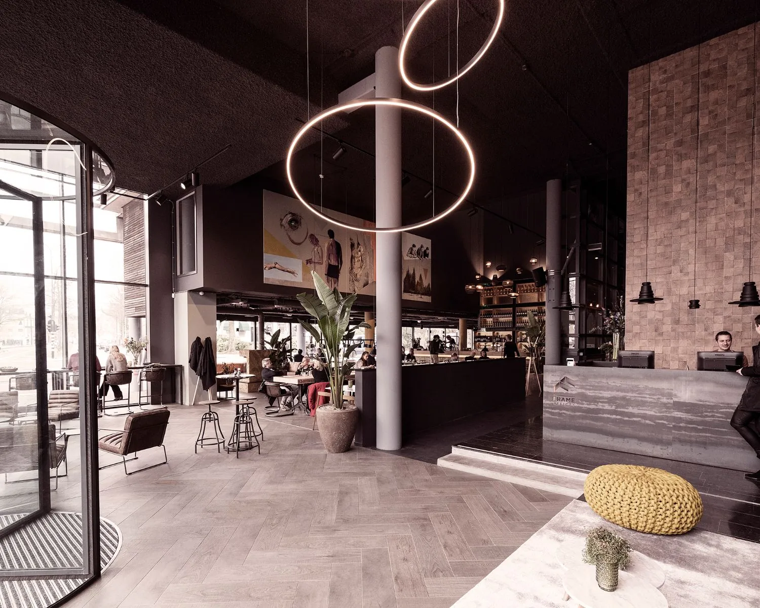 Modern ingericht hotel- of restaurantinterieur met hoge plafonds, een ronde lichtinstallatie en een receptiebalie.