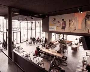 Interieur van een modern en sfeervol café met grote ramen, kunst aan de muur en gasten die aan tafels zitten.