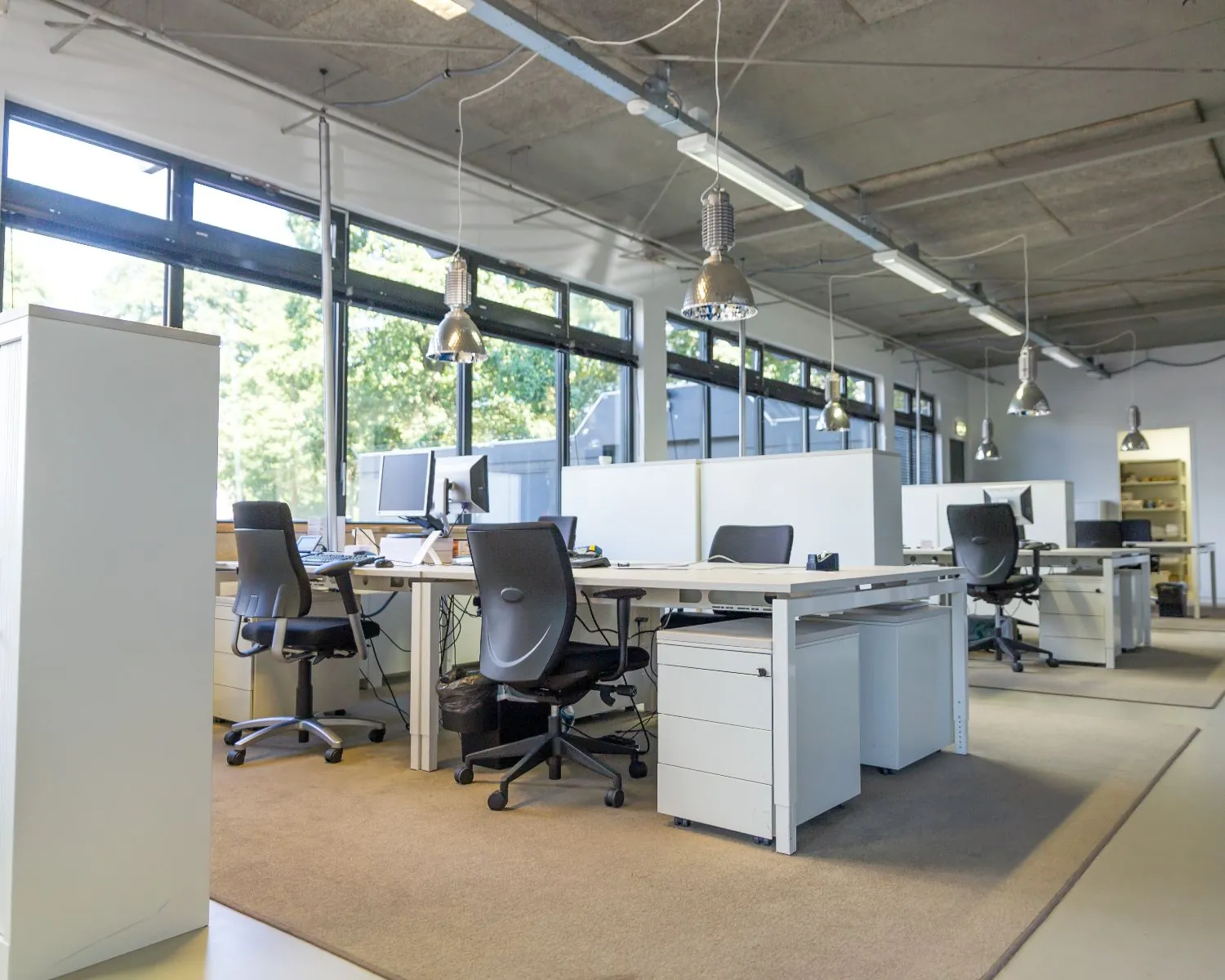 Moderne open kantoorruimte met bureaus, bureaustoelen, computers en grote ramen met daglicht.