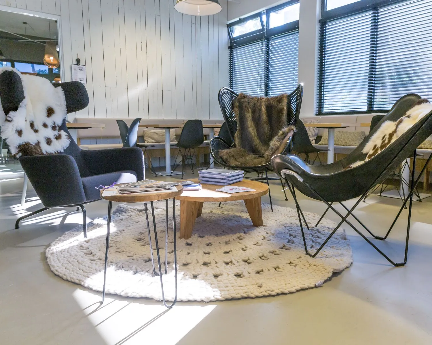 Gezellige zithoek met designstoelen, dierenhuidkleden en een ronde houten salontafel op een gebreid vloerkleed.