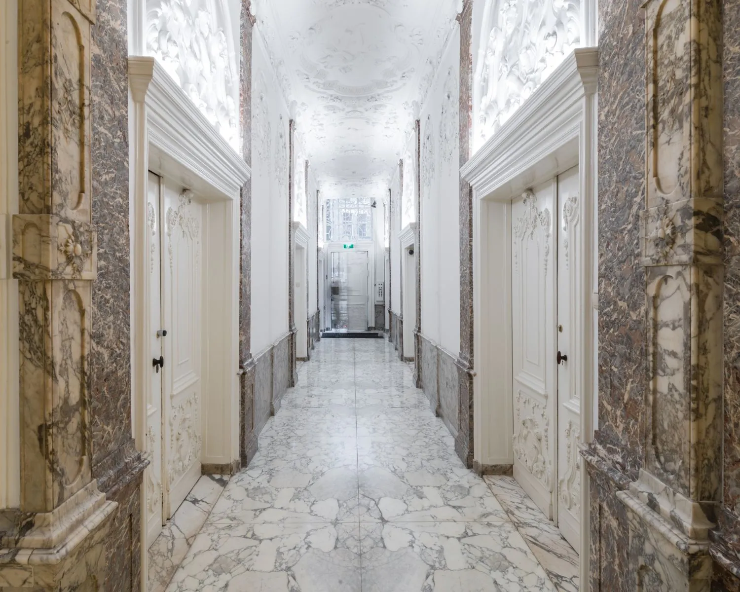 Luxe marmeren gang met decoratief stucwerk en dubbele deuren in een klassiek ingericht gebouw.