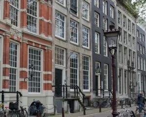 Gevels van traditionele Amsterdamse grachtenpanden met fietsen en lantaarnpalen op de stoep.