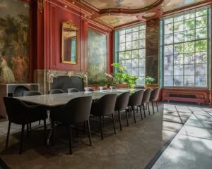 Luxe vergaderruimte met lange marmeren tafel, zwarte stoelen, grote ramen en klassieke muurschilderingen.