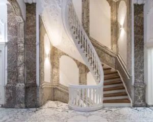 Marmeren trap met witte balustrade in een klassiek, rijk gedecoreerd interieur.