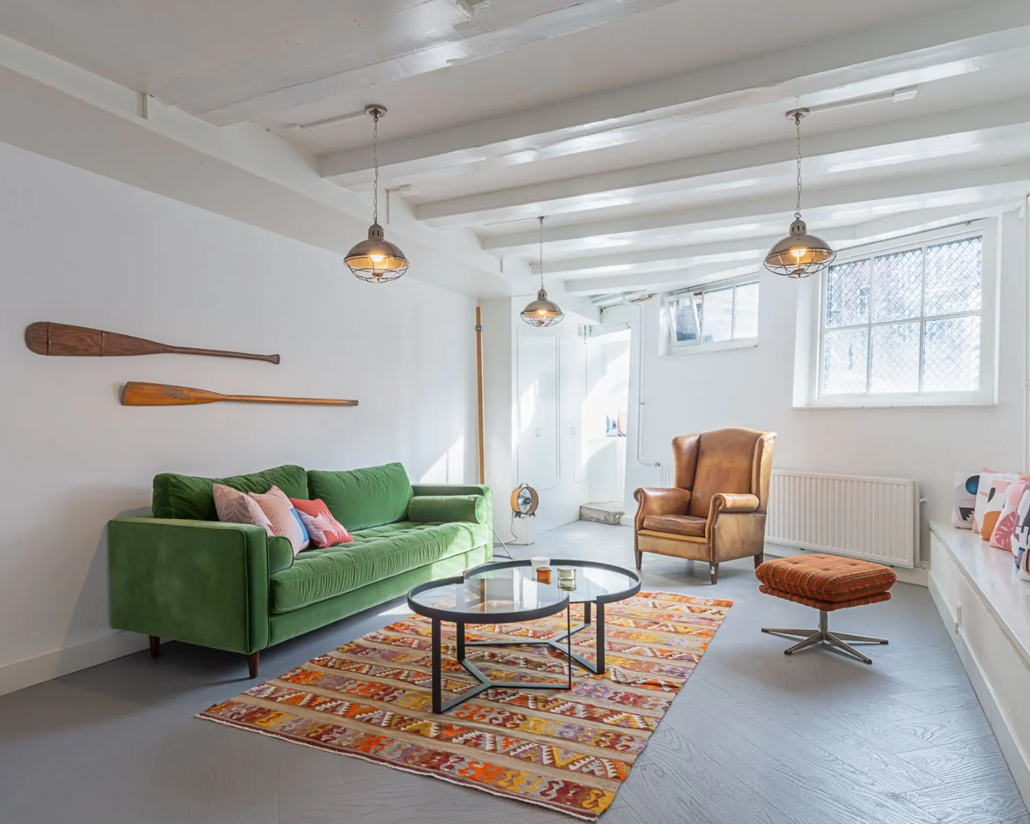 Lichte woonkamer met een groene bank, leren fauteuil, kleurrijk vloerkleed en decoratieve peddels aan de muur.
