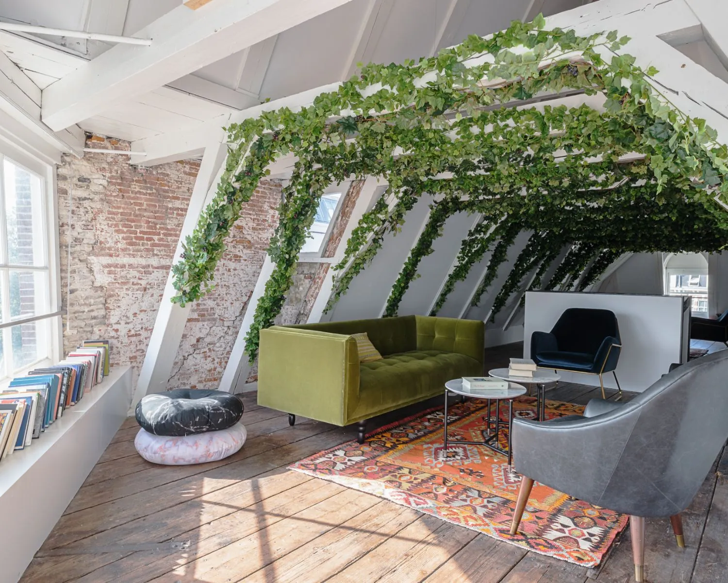 Sfeervol ingerichte zolderkamer met planten aan het plafond, een groene bank, kleurrijk vloerkleed en moderne zitmeubels.