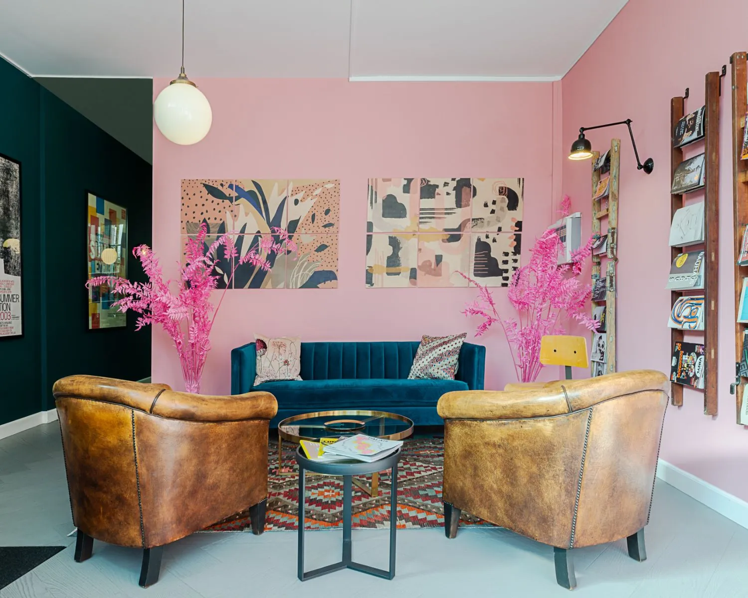 Stijlvol ingerichte zithoek met vintage leren fauteuils, een blauwe fluwelen bank en roze accenten tegen een roze muur.