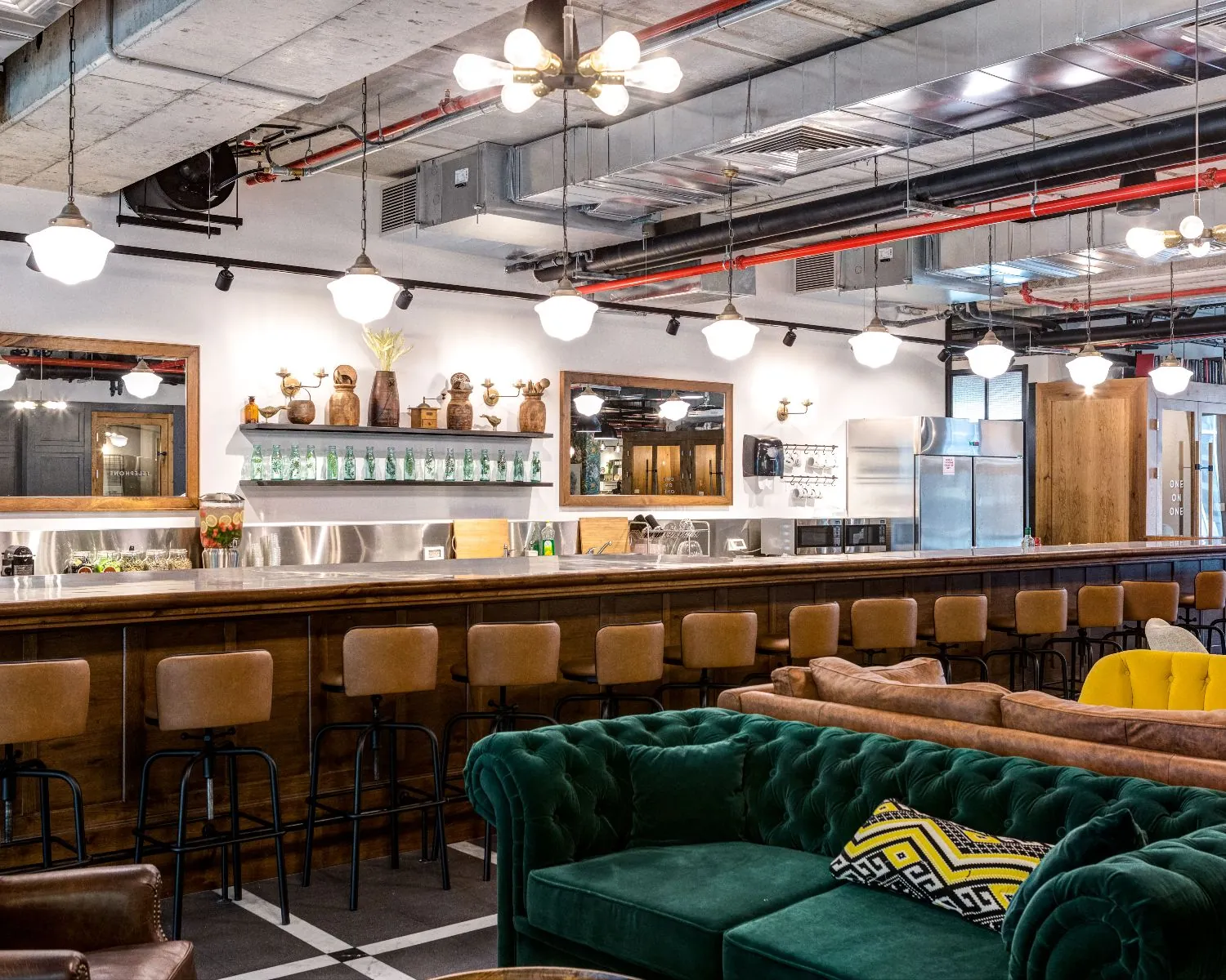 Moderne en sfeervol ingerichte bar met hoge barkrukken, industriële plafonddetails en kleurrijke zitbanken.