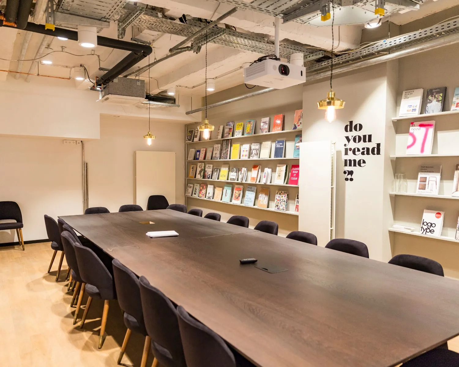 Moderne vergaderruimte met een lange tafel, zwarte stoelen en een muur vol design- en typografieboeken.