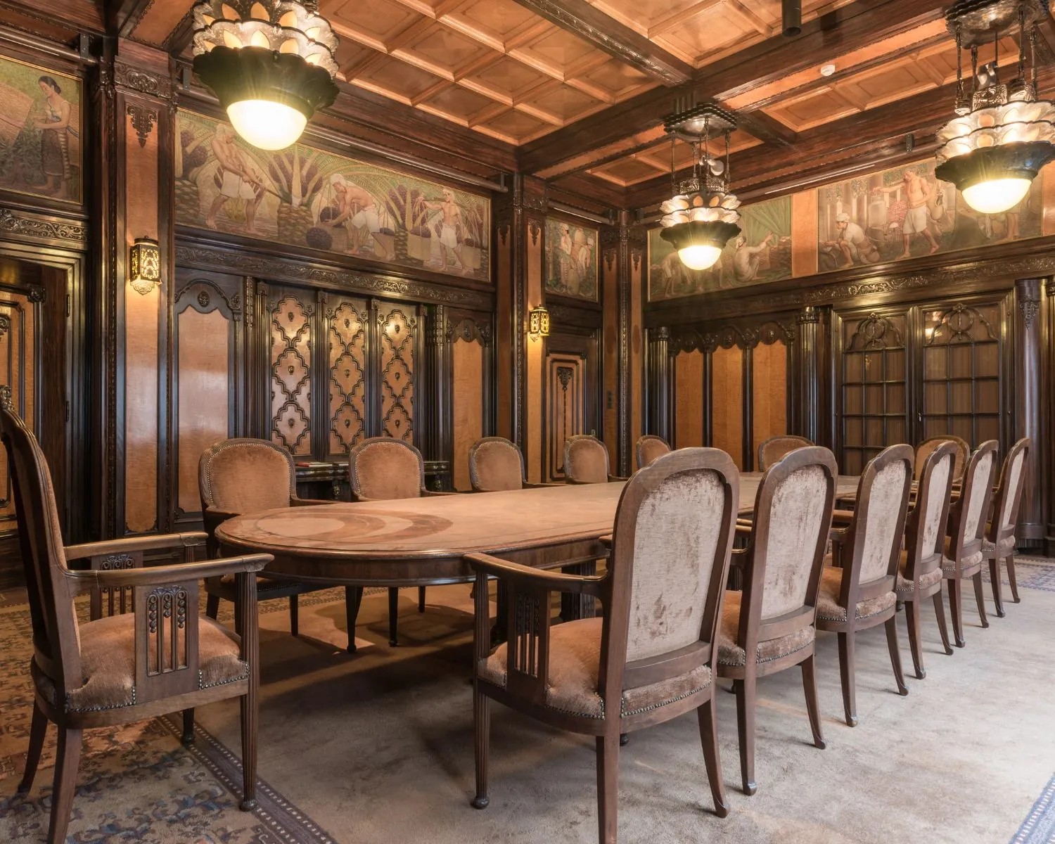 Vergaderzaal in klassieke stijl met houten lambrisering, muurschilderingen en een lange ovale tafel omringd door fluwelen stoelen.