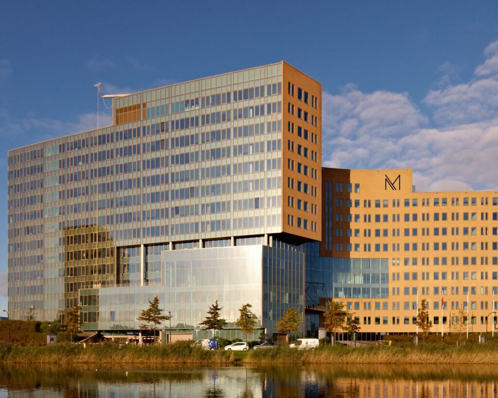 Modern kantoorgebouw met glasgevels en het logo van het gebouw "croped_1550150844", weerspiegeld in het water op de voorgrond.