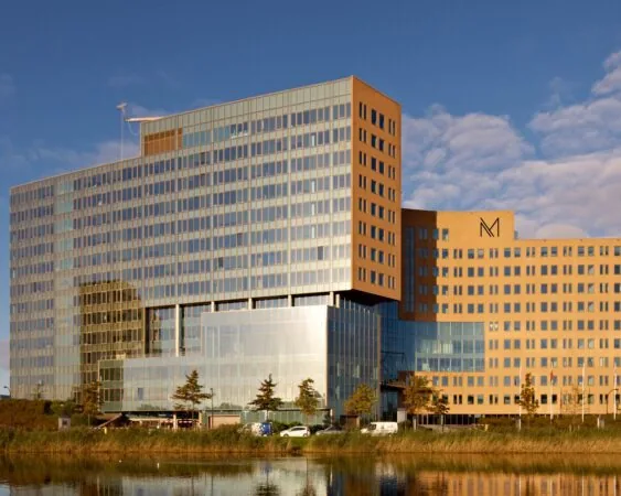 Modern kantoorgebouw met glasgevels en het logo van het gebouw "croped_1550150844", weerspiegeld in het water op de voorgrond.