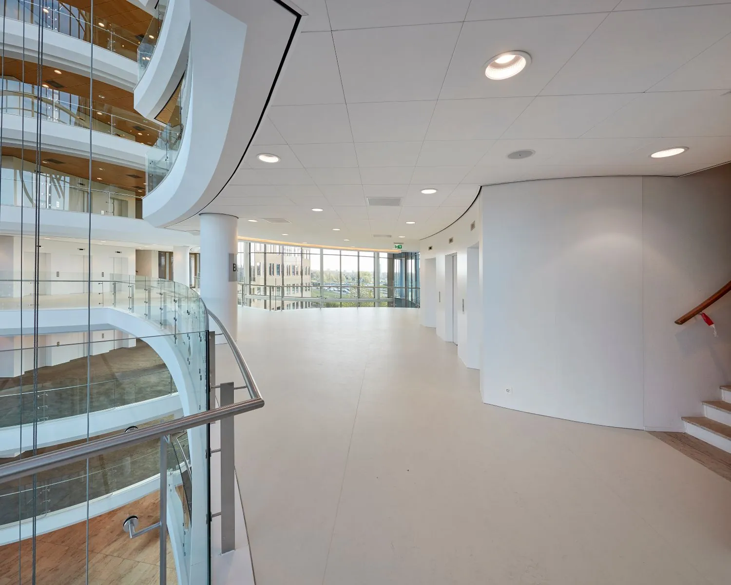 Ruim en modern ingericht kantoorgebouw met glazen balustrades en grote raampartijen.