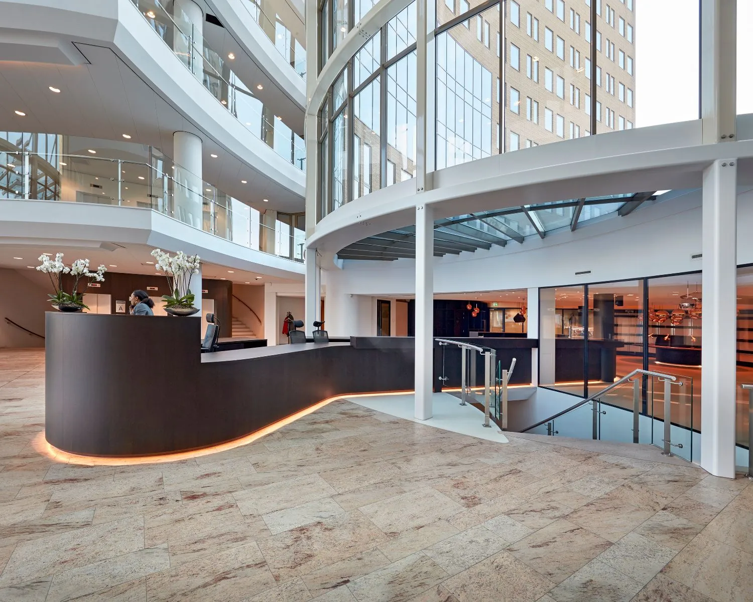 Moderne ingangshal met een gebogen receptiebalie, glazen gevel en meerdere verdiepingen.