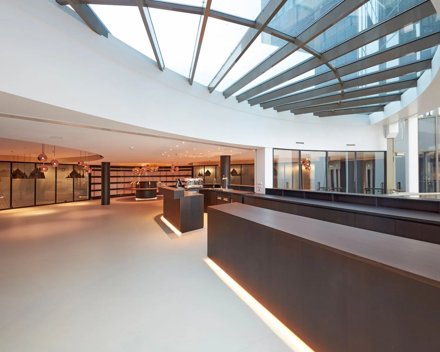 Moderne en ruime hotellobby met glazen dak en strakke houten receptiebalies.